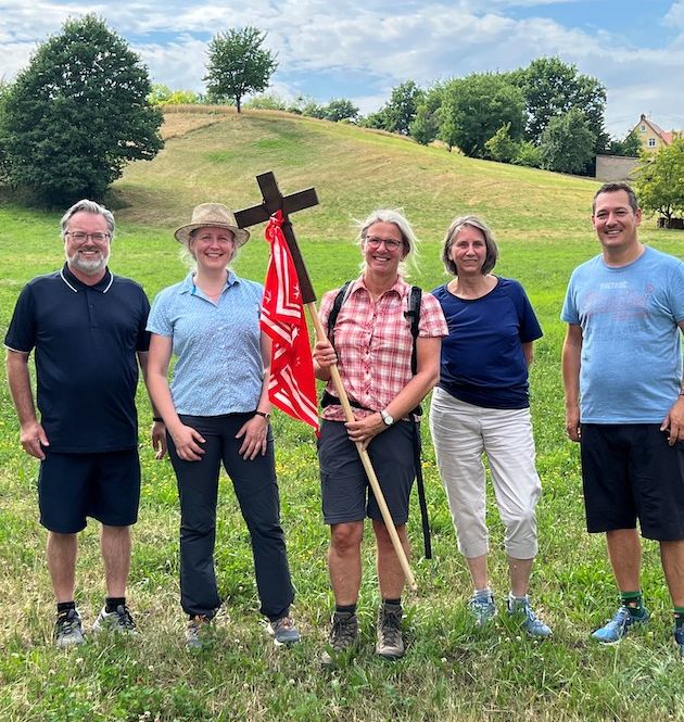 Gruppenbild mit Dörte Schrömges in der Mitte und 4 Teilnehmenden an ihrer Seite auf einer Wiese stehend mit einem Kreuz mit Malteser Tuch in der Hand