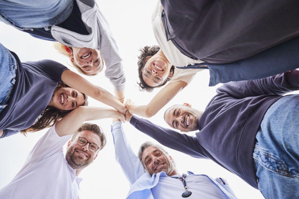 Sechs Personen legen sternförmig jeweils eine Hand aufeinander, von unten fotografiert.