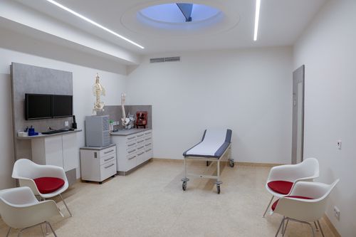 Untersuchungsraum mit Liege, Sitzgelegenheiten und medizinischen Modellen auf einem Unterschrank.