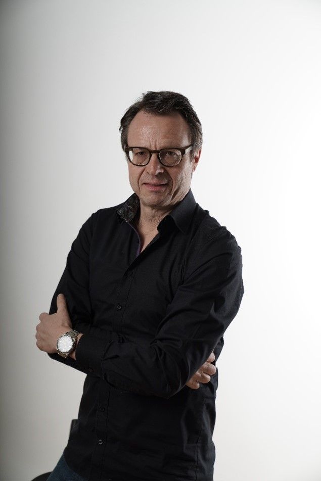 Ein Mann mit dunkler Kleidung, Brille und verschränkten Armen.