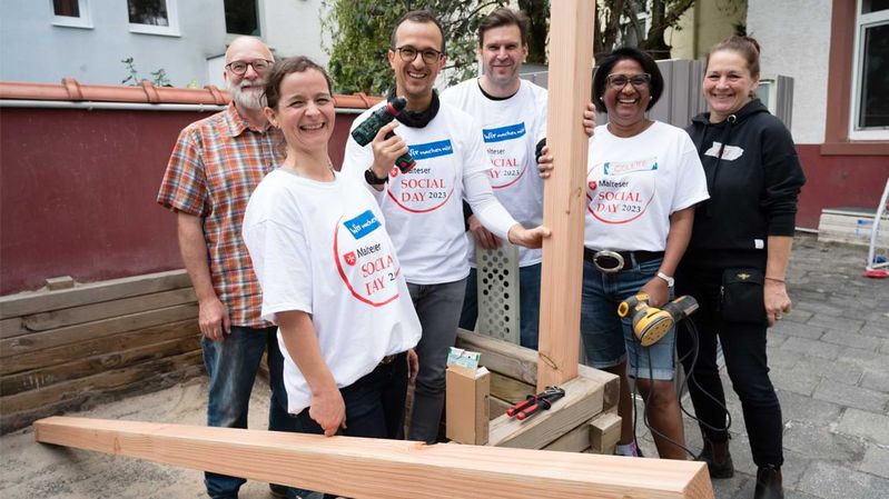 Eine Gruppe lächelnder Menschen mit Werkzeug und Holzbalken