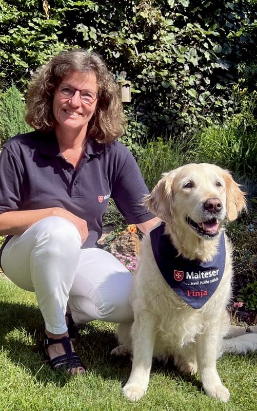 Frau (Malteser Mannheim) kniet neben Besuchshund Finja - ein Golden Retriever