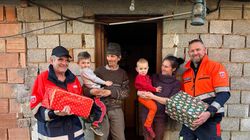 Zwei Mitarbeiter in Malteser-Kleidung stehen mit einer Familie mit zwei kleinen Kindern vor der Tür eines Hauses im Rohbau.