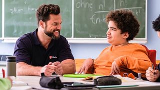 Malteser Schulbegleiter sitzt mit einem Jugendlichen im Rollstuhl im Klassenraum.