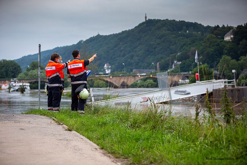 Zwei Menschen in Malteser Einsatzkleidung stehen am Hochwasser 