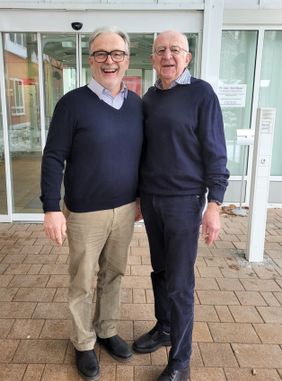 Zwei ältere Männer stehen vor einem Klinikgebäude mit automatischer Glastür.