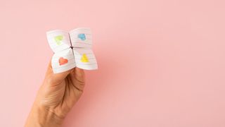 Eine Hand mit einem Himmel und Hölle-Spiel vor rosa Hintergrund