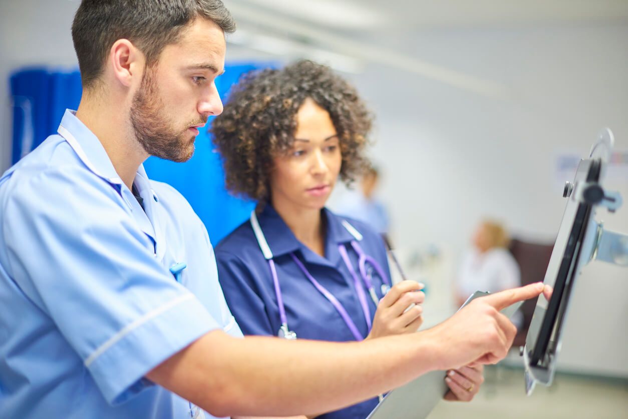 Unter Aufsicht einer Krankenpflegerin bedient ein Krankenpflegerazubi einen Klinikmonitor.