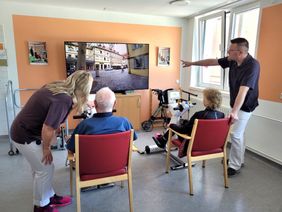 Zwei Therapeuten mit zwei Senioren blicken auf einen Bildschirm.