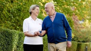 Malteser Mitarbeiterin begleitet älteren Mann bei einem Spaziergang.