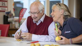 Älterer Mann und Helferin der Malteser schälen fröhlich Kartoffeln