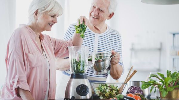 Zwei alte Menschen mixen einen grünen Gemüsesmoothie 