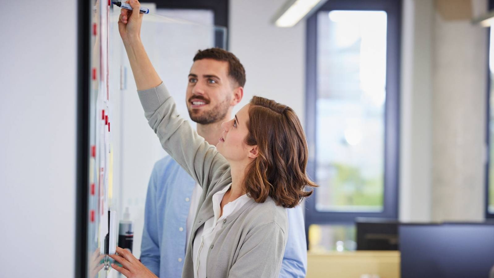 Mann und Frau stehen in einem Büro vor einem Whiteboard und arbeiten