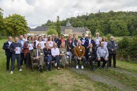 Alle Teilnehmenden des Gipfels stehen oder Sitzen auf zwei Holzbänken zusammen für ein Gruppenfoto vor der Kulisse on Schloss Ehreshoven.