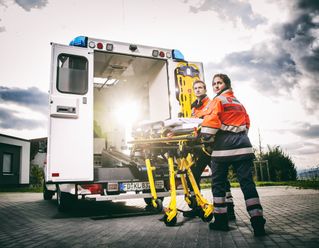 Zwei Mitarbeiter des Malteser Hilfsdienstes schieben eine Trage in einen Rettungswagen