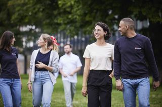 Eine Gruppe junger Malteser Mitarbeitenden, jeglichen Aussehens und Geschlechts, schlendern lachend über eine Grünfläche.