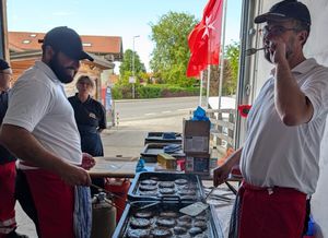 Zwei Helfer stehen an einem Grill und braten Fleisch