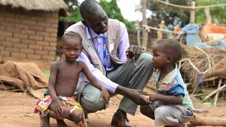 Ein Mitarbeiter für Malteser International unterhält sich mit zwei afrikanischen Kindern in ihrem Dorf.