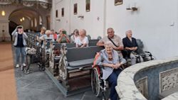 Ältere Menschen sitzen in Kirchenbänken und bestaunen den Kirchenbau um sich herum.