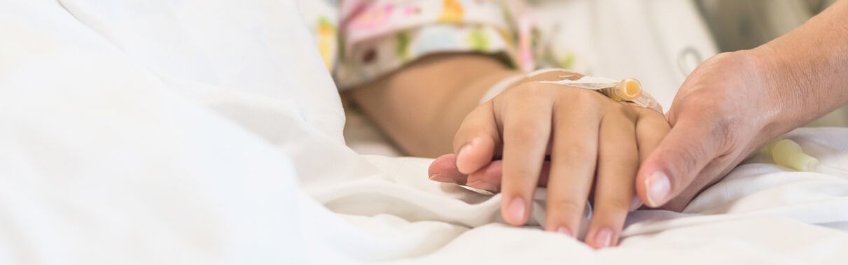 Pflegekraft hält die Hand eines bettlägerigen Kindes.