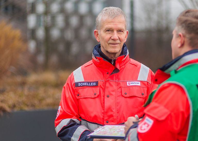 Ein Mann in seinen 60ern steht in Einsatzkleidung im Freien. 