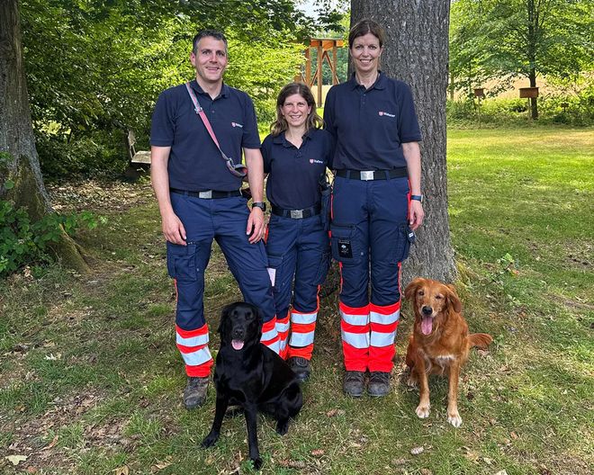 Abgebildet sind drei Personen in Einsatzbekleiung des Malteser Hilfsdienst sowie zwei Hunde, die die Prüfung als Kadaverspürhunde erfolgreich abgelegt haben.