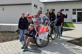 Mehrere Malteser Ehrenamtliche stehen draußen mit einer Fahrrad-Rikscha