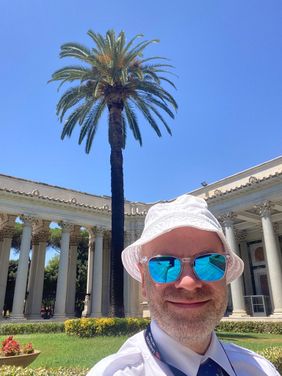 Dr. Stefan Tomaselli steht vor einer Palme und einem alten Gebäude mit Säulen