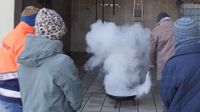 Ein Mann löscht ein Feuer in einer Feuerschale, während ein Malteser Ausbilder und weitere Kursteilnehmende zuschauen.