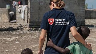 Mitarbeiterin von Malteser International mit zwei schwarzen Kindern an der Hand. 