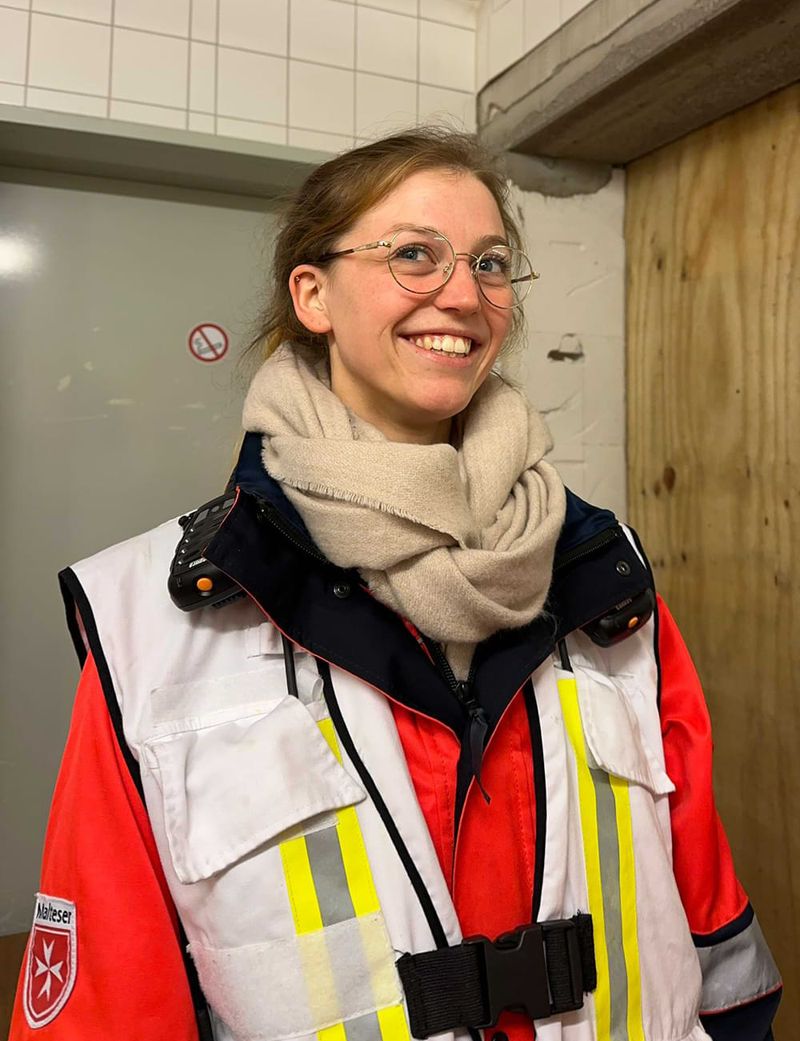 Eine lächelnde junge Frau mit Brille in Einsatzkleidung der Malteser in Deutschland