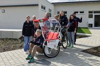 Mehrere Malteser Ehrenamtliche stehen draußen mit einer Fahrrad-Rikscha