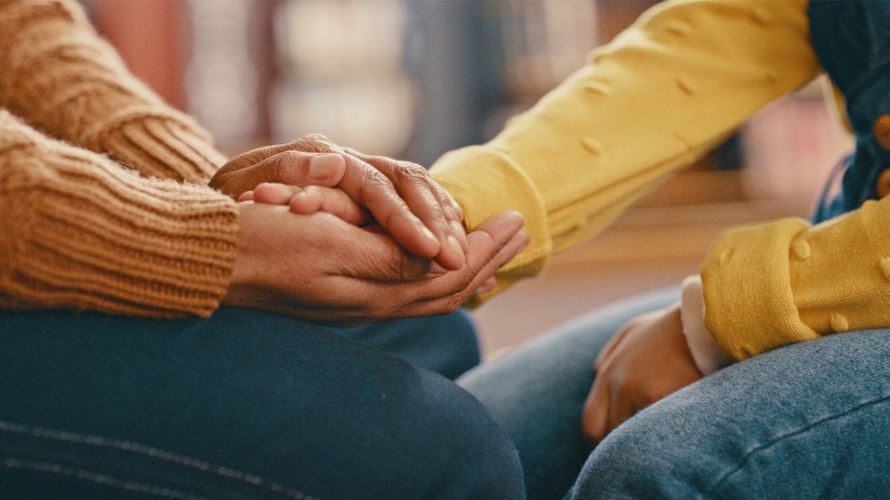 Die beiden Hände einer Person halten unterstützend die Hand einer anderen Person.