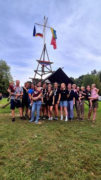 Gruppenfoto von zwanzig Jugendlichen und Gruppenleitungen der Malteser Jugend, die auf einer Wiese vor einem Bannermast stehen. Auf dem Banner steht Bunte Bande.