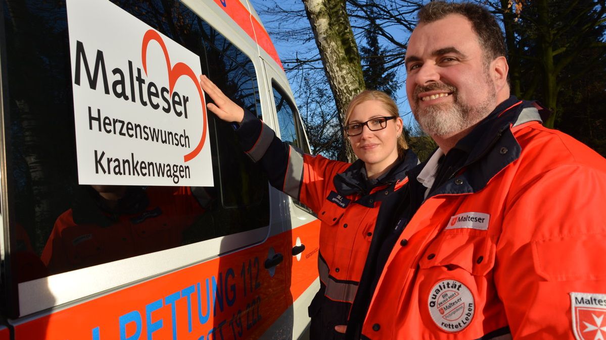 Ehrenamtliche des Projekts Malteser Herzenswunsch Krankenwagen stehen vor einem Krankenwagen.