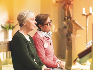 Junge Frau mit Malteser Halstuch ist mit einer älteren Person in einer Kirche