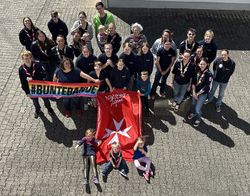 Gruppenfoto von der Delegiertenversammlung auf dem ca. 35 Kinder, Jugendliche und Erwachsene zu sehen sind. Vor der Gruppe liegt ein Malteser Jugend Banner.