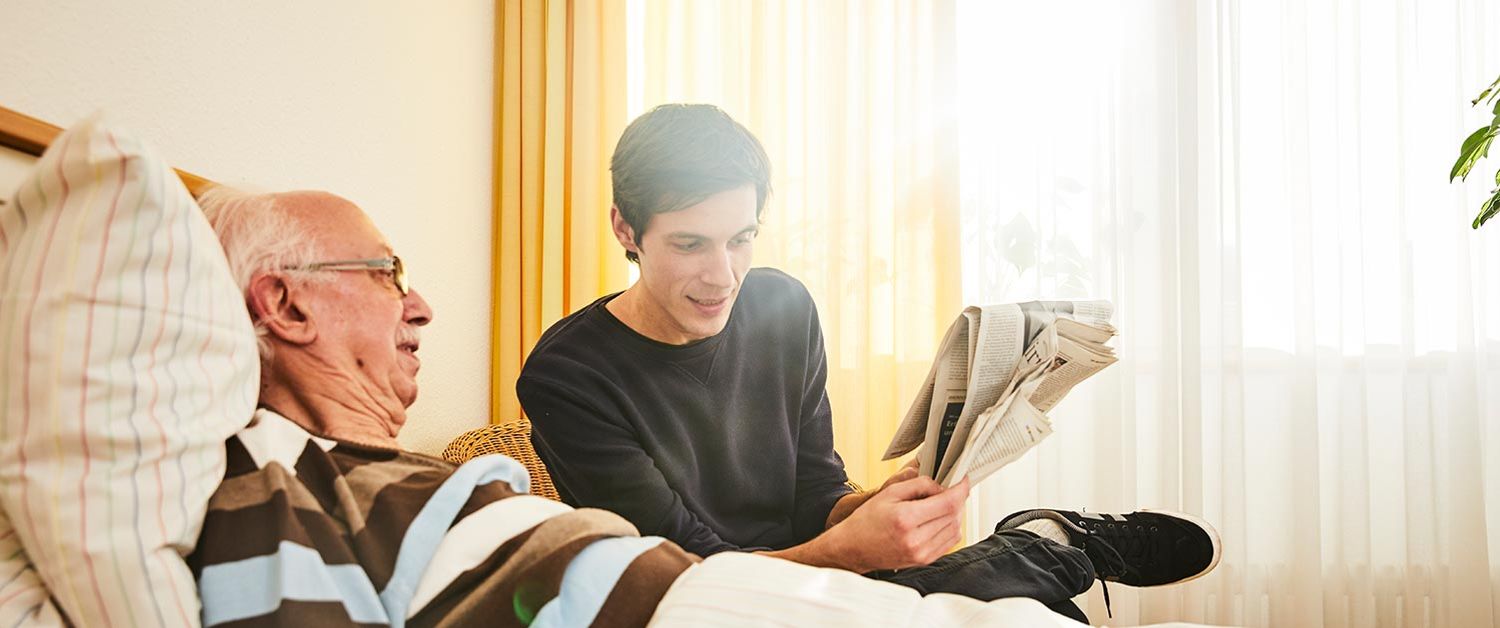 Ein junger Mann sitzt neben einem alten Mann, der im Bett liegt
