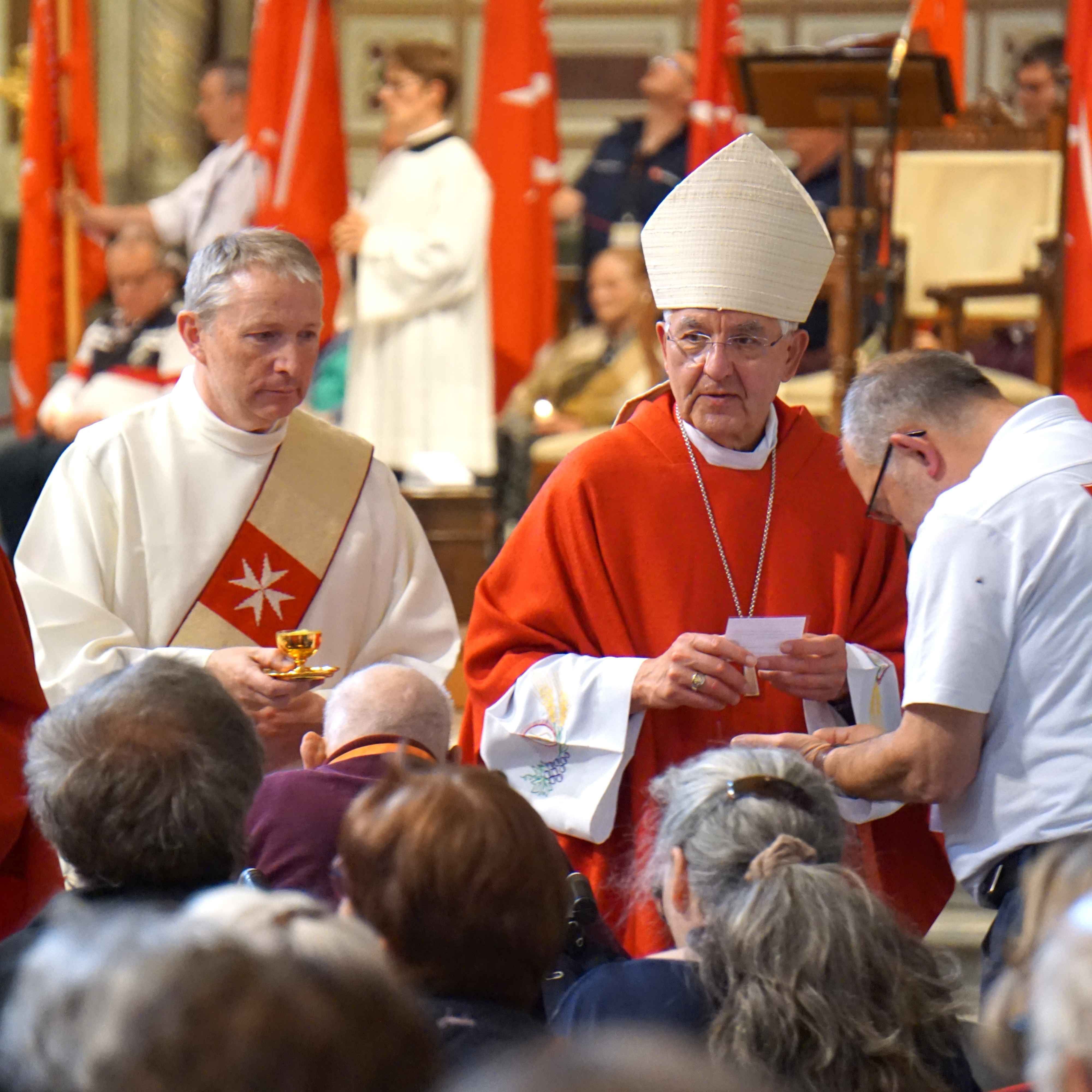 Zwei Geistliche in liturgischer Kleidung, einer mit rotem Gewand und Mitra, der andere mit weißem Gewand und rotem Kreuz, vor einer versammelten Gemeinde im Lateran.