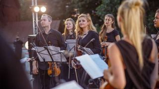 Mehrere Mitglieder eines Orchesters stehen auf einer Outdoo-Bühne