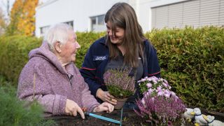 Ältere Frau arbeitet mit Malteser Helferin im Garten