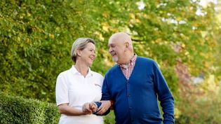 Malteser Mitarbeiterin begleitet älteren Mann bei einem Spaziergang.