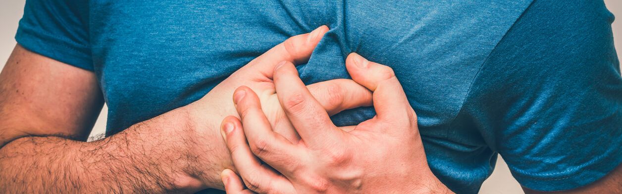 Mann im blauem T-Shirt fasst sich mit beiden Händen krampfhaft ans Herz