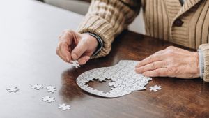 Älterer Mensch sitzt an einem Holztisch und setzt ein kopfförmiges Puzzle zusammen.