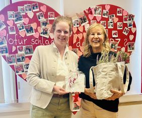 Zwei Frauen stehen vor einem roten Herz, in den Händen halten sie Geschenke