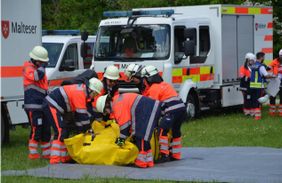 Mehrere Personen in Malteser Einsatzkleidung beim Aufbau eines Sanitätszeltes. Einsatzwagen im Hintergrund