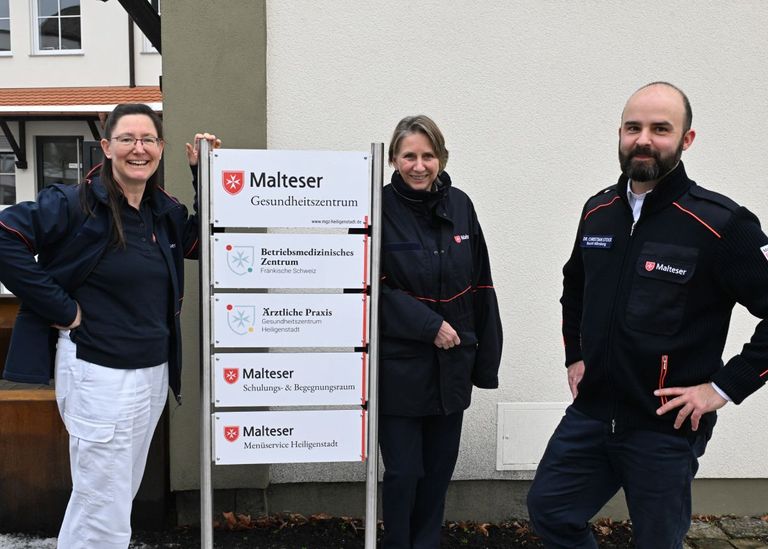 Drei Personen an einer Stele mit Beschreibung des Gebäudes hinter ihnen
