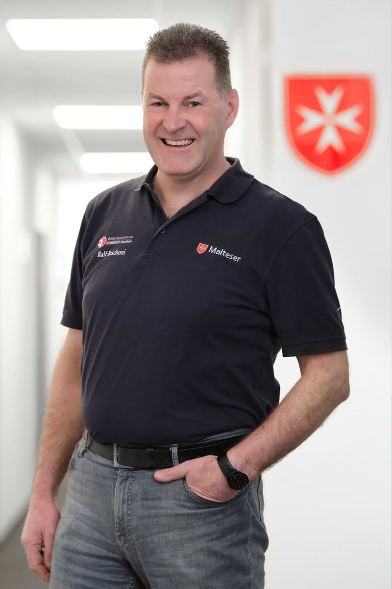 Porträt eines lächelnden Mannes mittleren Alters, der eine Hand in der Hosentasche hat.