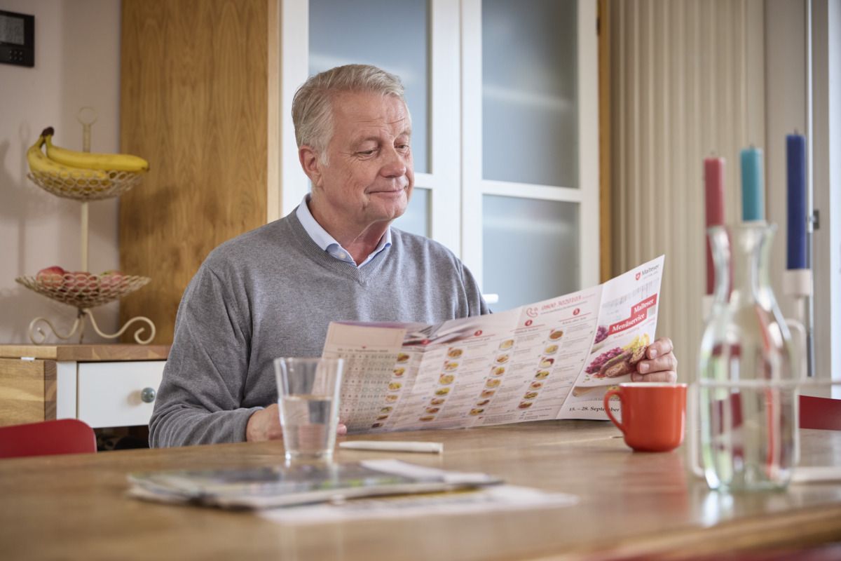 Ein Mann stöbert den Menükatalog des Malteser Wochenkartons durch.