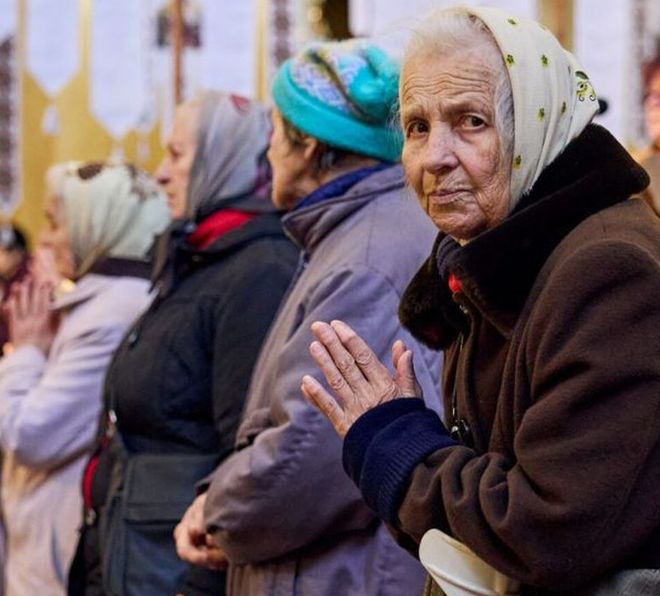 Eine ältere Frau ist gestützt auf eine Gehhilfe und betet. Foto: Malteser Ukraine